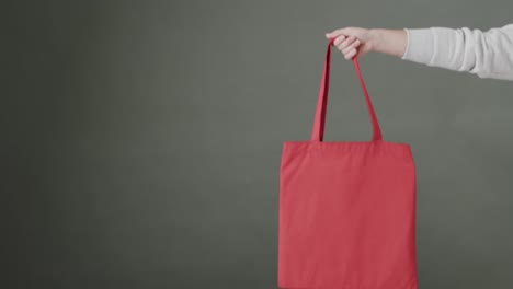 Hand-of-caucasian-woman-holding-red-bag-on-grey-background,-copy-space,-slow-motion