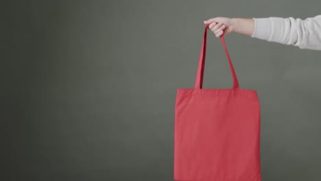 mano de mujer caucásica sosteniendo una bolsa roja en fondo gris, espacio de copia, cámara lenta