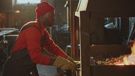 african american blacksmith heating metal rod in forge fire