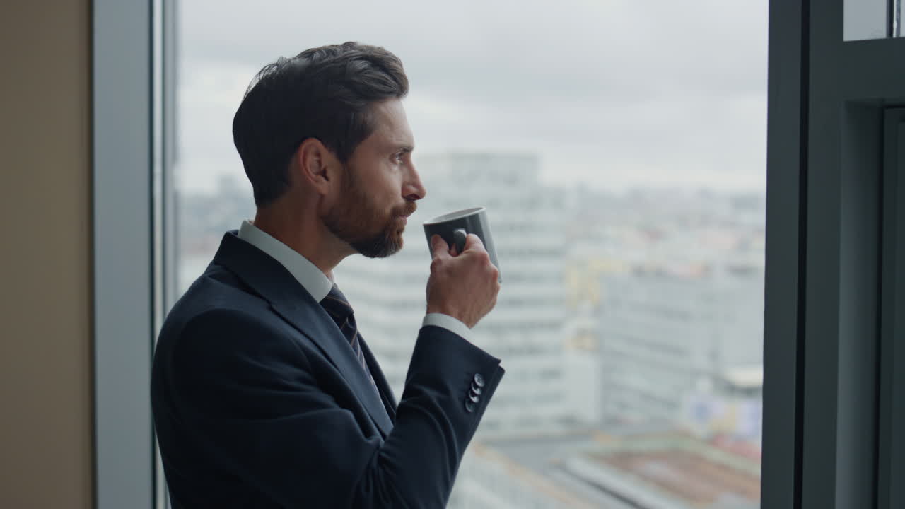 CEO manager che si gode la pausa caffè in piedi alla finestra dell'ufficio, in primo piano. Uomo che beve.
