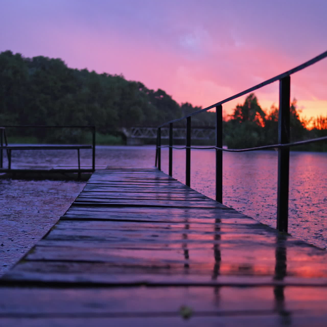 Heavy rain with small lightning over the river. Long footbridge in the river during the rain in the evening in summer. Beautiful natural background at sunset with rainy drops outdoors.