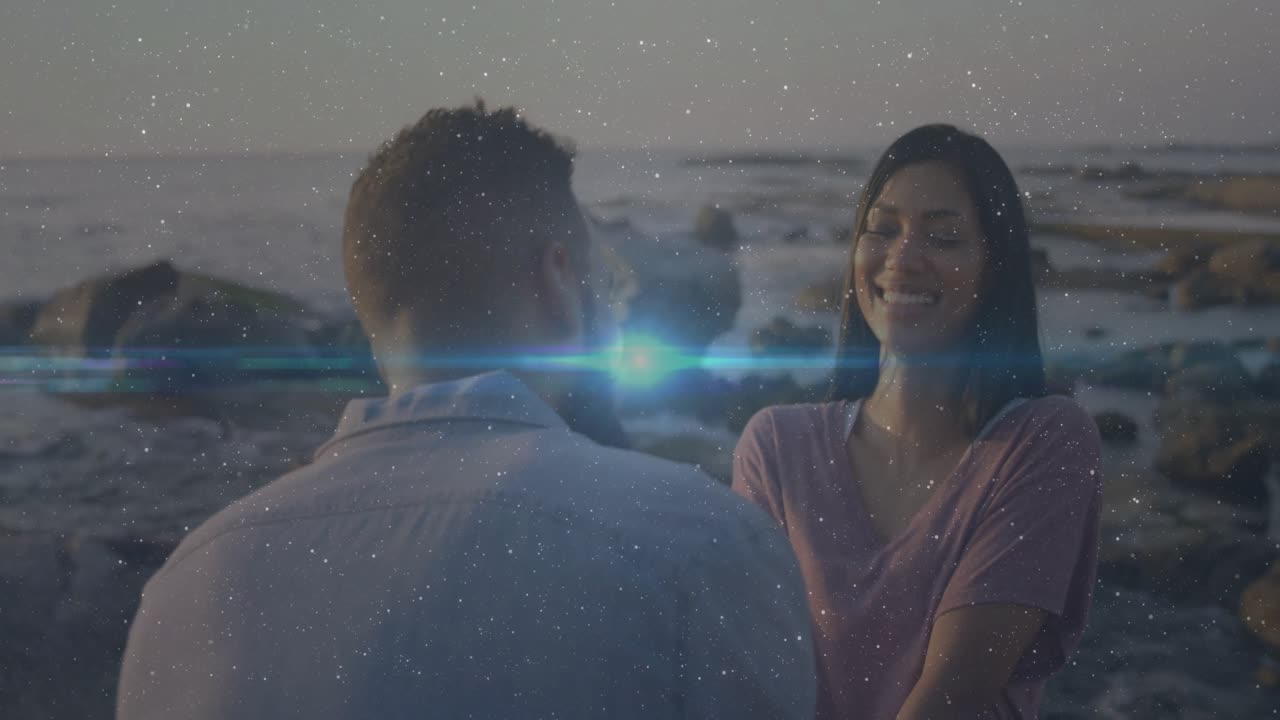 Bearded man speaking softly on sunset shore, causing laughter while lens flare appearing
