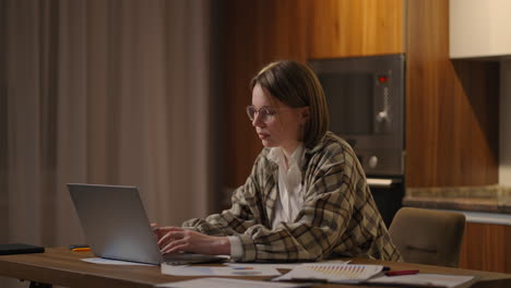 a girl works from home or a student is studying from home or a freelancer. she uses a laptop and a phone. girl sit at desk in living room study on laptop making notes concentrated young woman work