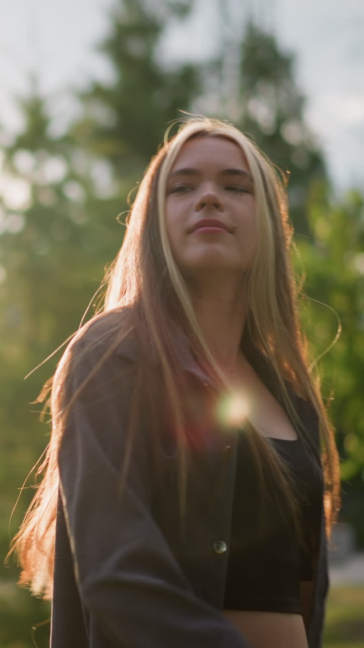dama girando alegremente en el sentido de las agujas del reloj en el campo de hierba mientras tira su cabello hacia atrás, la luz del sol creando una atmósfera radiante a su alrededor, el fondo incluye vegetación, árboles y un edificio