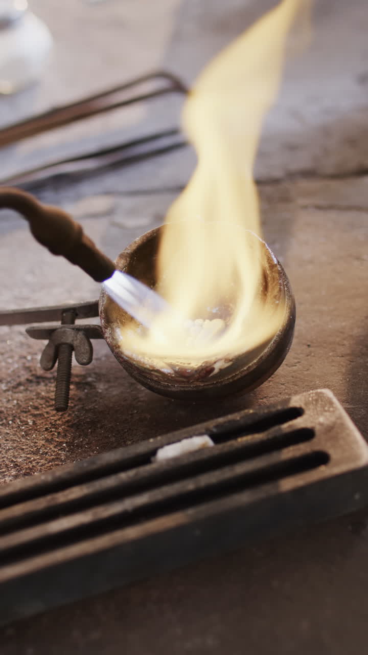 Vertical video of close up of melting metal with blowtorch in workshop in slow motion