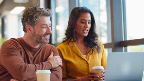 mature male businessman brings takeaway coffee for female colleague as they have meeting with laptop