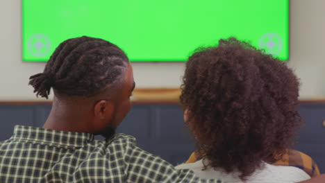 rear view of multi-generation family sitting on sofa at home watching green screen tv and laughing at comedy - shot in slow motion