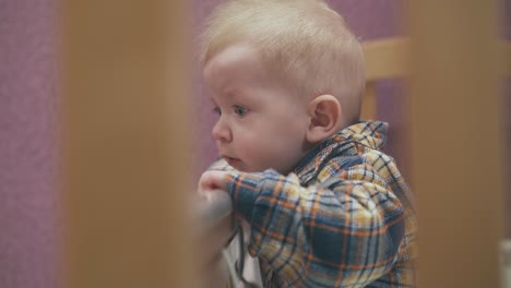 un niño pequeño con ojos azules se apoya en el borde de una cama de madera