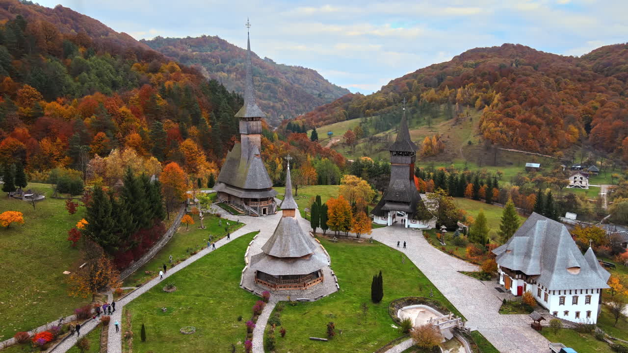 Aerial drone view of the Barsana Monastery, Romania. Main church and other buildings, visitors, hills covered with yellowing forest around