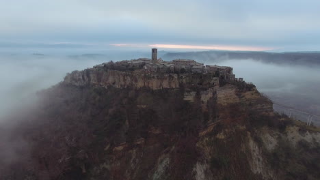 aerial dolly shot of civita di bagnoregio in the middle of the clouds at dusk. lateral shot revealing the old city. 4k