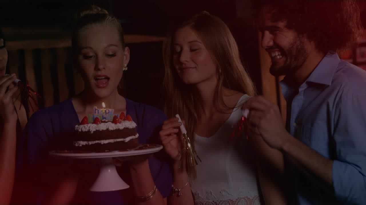 Cake-holder in purple inhaling blowing candles for birthday on deck guests blowing horns red flares