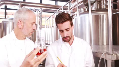 dos hombres en bata de laboratorio mirando el vaso con cerveza