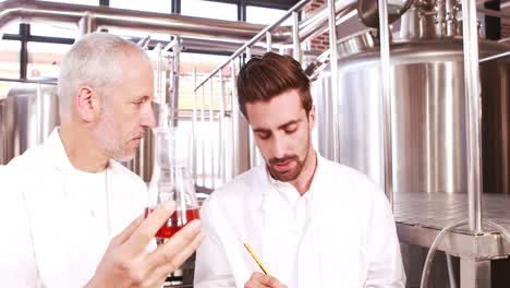 two men in lab coat looking at the beaker with beer