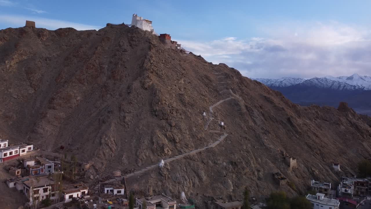 vista aérea cinematográfica que revela el monasterio y el templo de sankar con vistas a la ciudad de leh con la vista de la cordillera nevada en el fondo durante la puesta de sol, jammu y cachemira, india