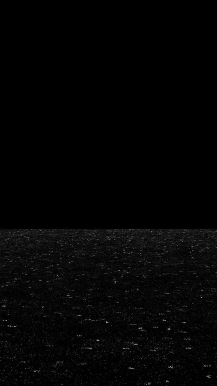 Pluie tombant sur une surface d'asphalte ou de rue mouillée la nuit, créant un arrière-plan sombre et cinématographique avec une ligne d'horizon.