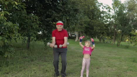 Granddaughter-and-grandfather-doing-fitness-exercises-with-dumbbells.-Senior-man-with-child-kid-girl