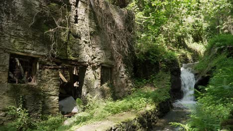 Vista-De-Una-Vieja-Casa-Abandonada-Que-Se-Está-Desmoronando-En-El-Bosque,-Cerca-De-Una-Pequeña-Cascada