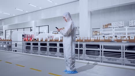 full body side view of asian male scientist using smartphone while standing with conveyor for packaging coffee beans in bags at coffee factory
