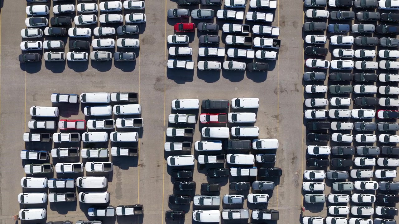 Adskillige splinternye erhvervsvarevogne parkeret i ordnede rækker ved et fabriksdistributionscenter, der venter på salg eller forsendelse, hvilket repræsenterer bilindustrien og koncepter for masseproduktion.