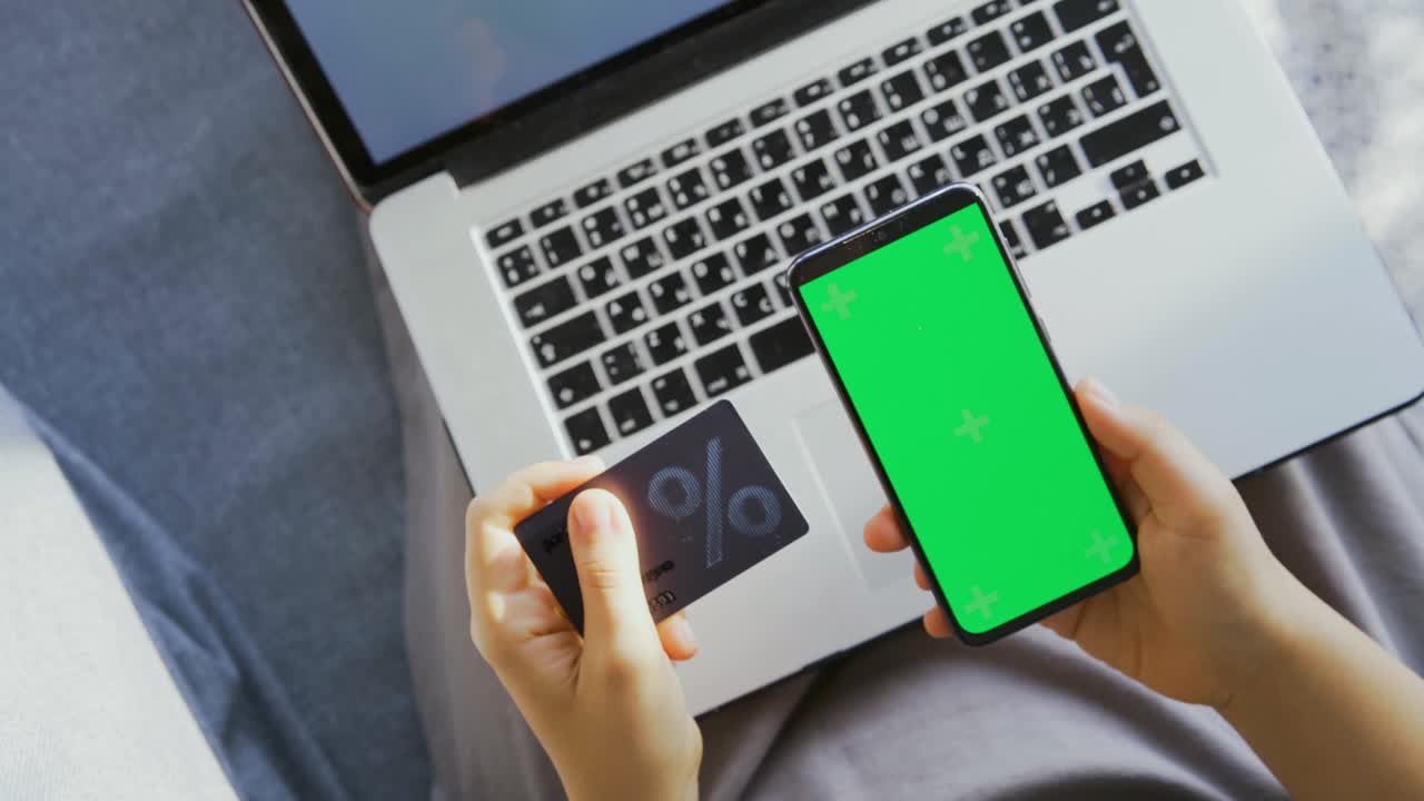 여자 는 노트북 위 에 할인 카드 와 휴대 전화 를 들고 있다