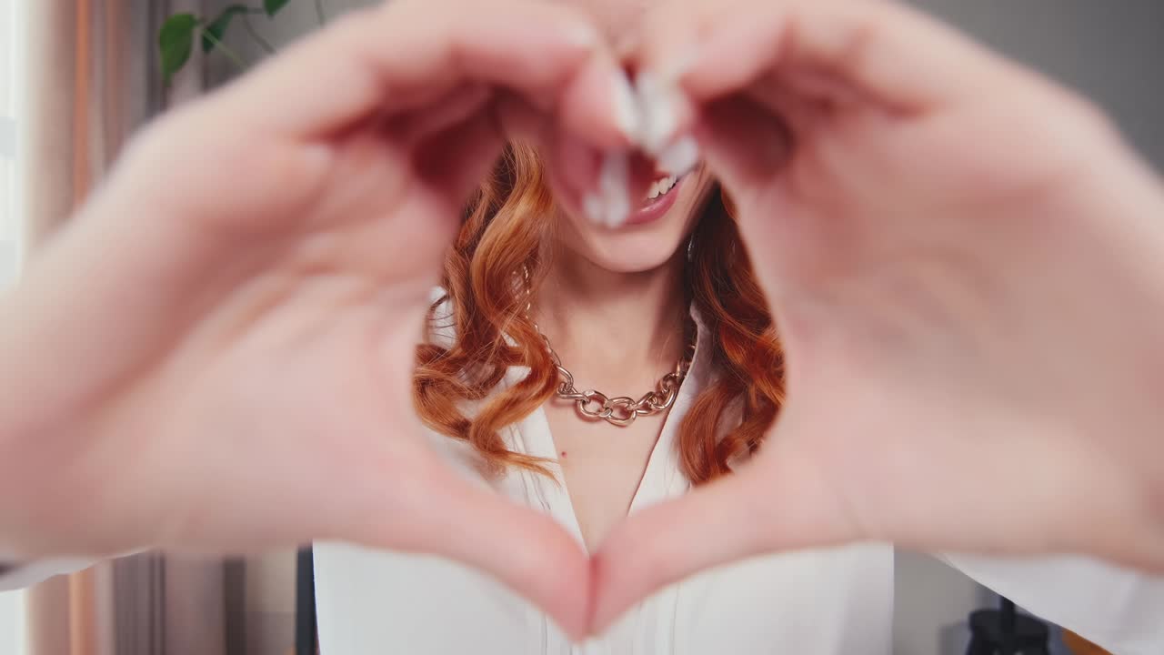 Happy redhead caucasian woman millennial smiles and shows heart made of fingers