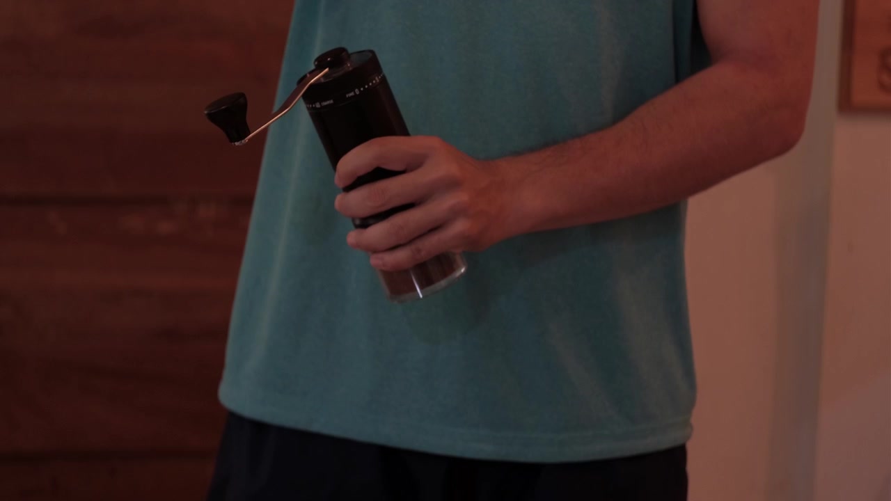 Mezza figura di un giovane uomo che macina il caffè in casa con un macinacaffè manuale portatile, mostrando un semplice processo di preparazione del caffè fatto in casa