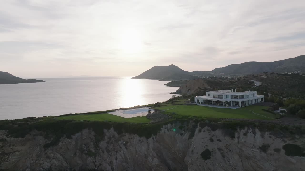 Aerial flyover with villa and swimming pool and coastline during sunset time in Greece