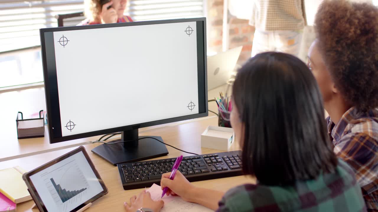 Due imprenditrici diverse e felici che usano il computer in un ufficio informale, con spazio per il testo sullo schermo, al rallentatore.