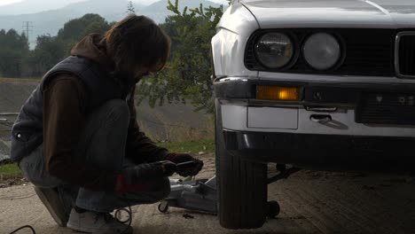 mechanic man quickly removes tire from white car with impact wrench