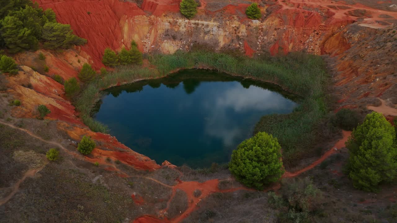 отранто, пулья, италия - живописный вид на бокситовую пещеру, с ее озером, окруженным зеленым, и облачным небом, отражающимся на воде - воздушный снимок