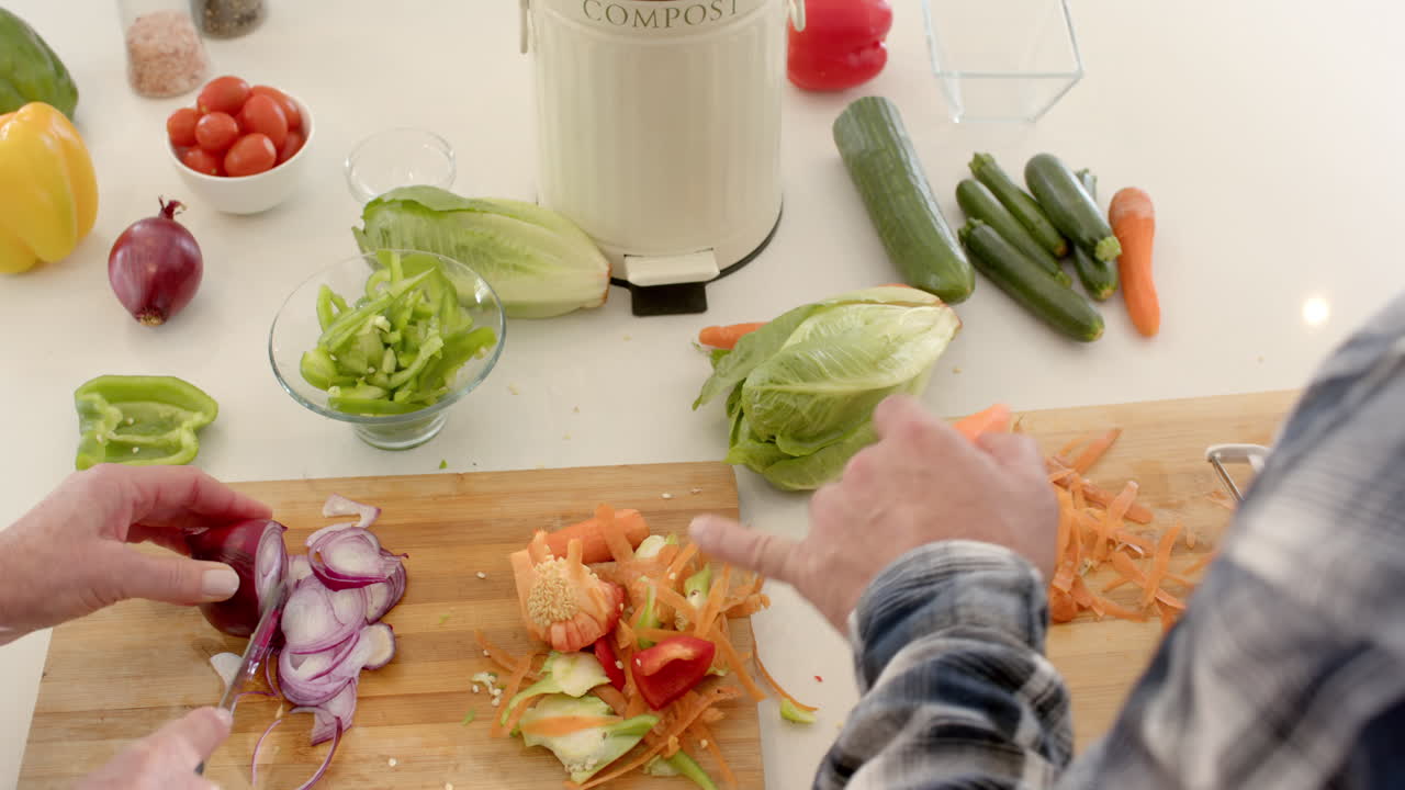 Chopping fresh vegetables in kitchen, preparing healthy meal with compost bin nearby