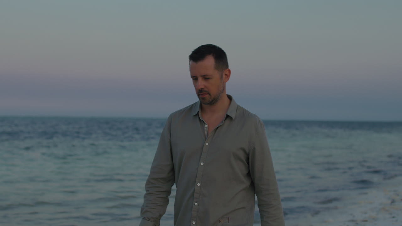 Thoughtful lonely man walk along the tropical beach in silence, contemplating his pas, present and future life during the sunset.