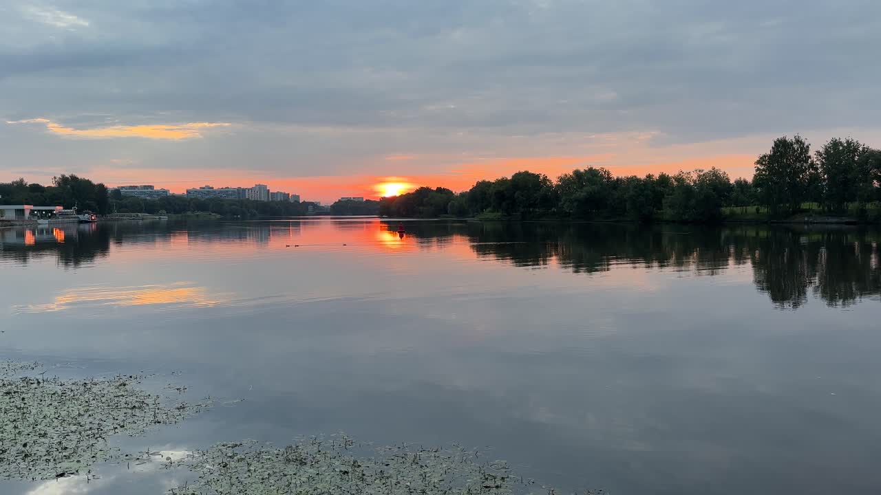 A quiet dawn in the city with gray clouds and a red sun over the river (4K60)