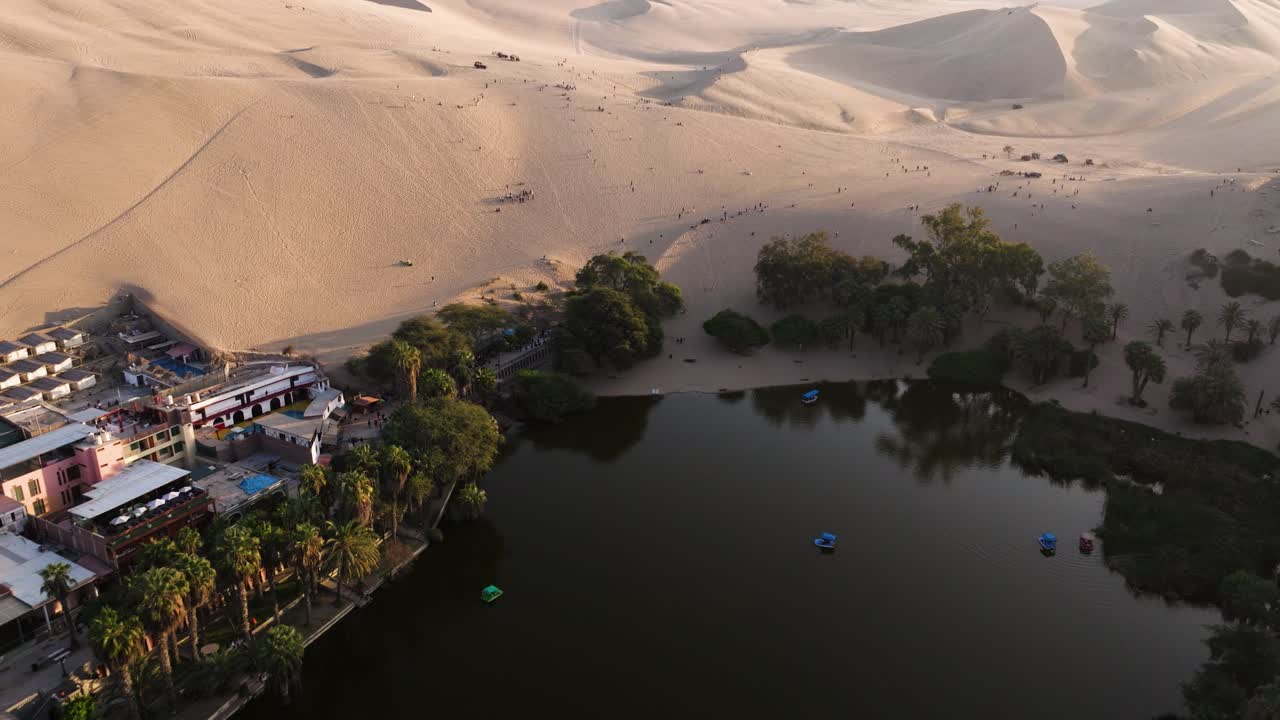Aerial dolly over Huacachina oasis lake framed by desert dunes under soft evening light, wanderlust exploration