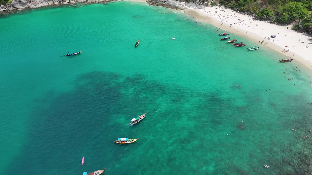 Aerial footage captures vibrant beach and water activities in Phuket, Thailand, showcasing boats, swimmers, and stunning turquoise waters