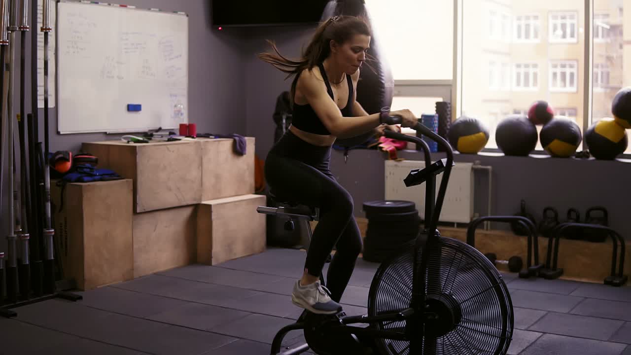 Attractive brunette girl with sportive body wearing dryfit sportswear working out on stationary bike. Fitness and wellbeing.