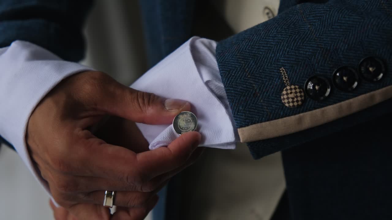 Stylish close-up of a groom fixing his cufflinks and adjusting his blue suit jacket over a crisp white shirt. Elegant moment symbolising confidence, style, and preparation for the big day