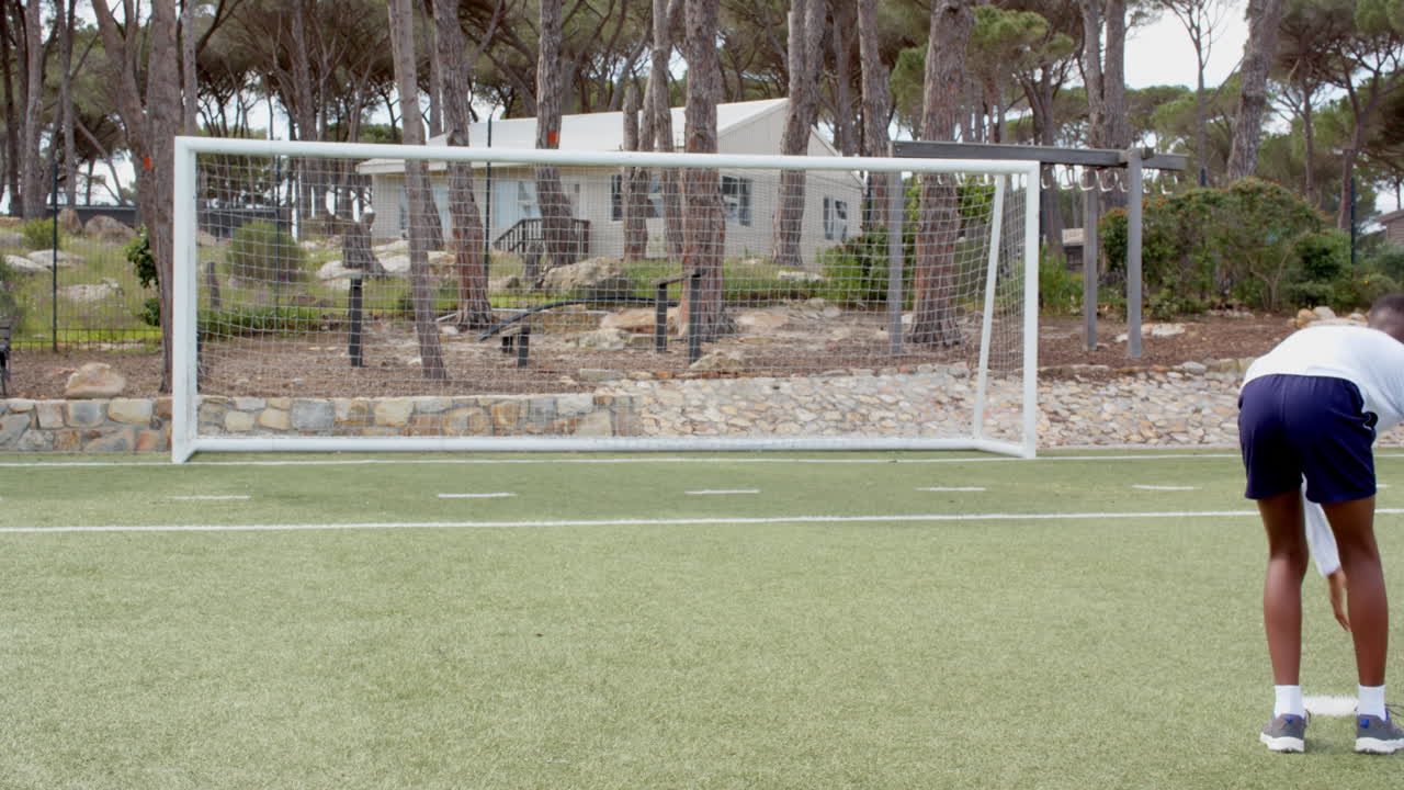 Playing soccer on field, boy in athletic gear near goalpost, enjoying game