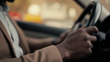 Close-up-shot-of-a-man-Businessman-with-Black-skin-color-in-a-brown-jacket-holds-with-his-two-hands-the-steering-wheel-of-a-modern-car-while-he-is-driving-in-a-car-in-a-modern-salon-during-a-business-trip-in-the-city