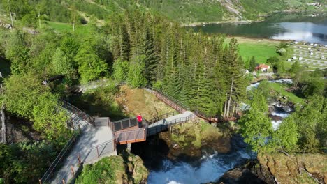 one man standing on geiranger river viewpoint above waterfall - aerial view unweiling geiranger fjord in background