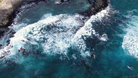 drone pans across ocean white wash at a rocky beach with birds eye view