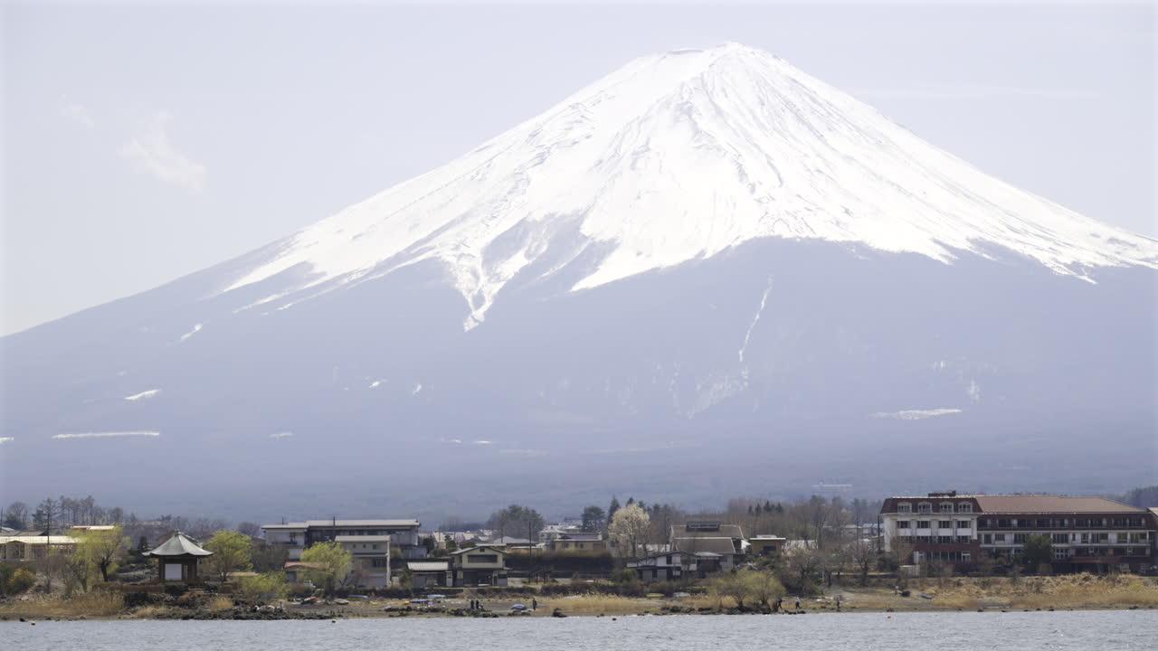 Mount Fuji stands majestically with snow-capped peaks above lakeside in Japan. Clear spring skies provide a stunning backdrop to this serene landscape