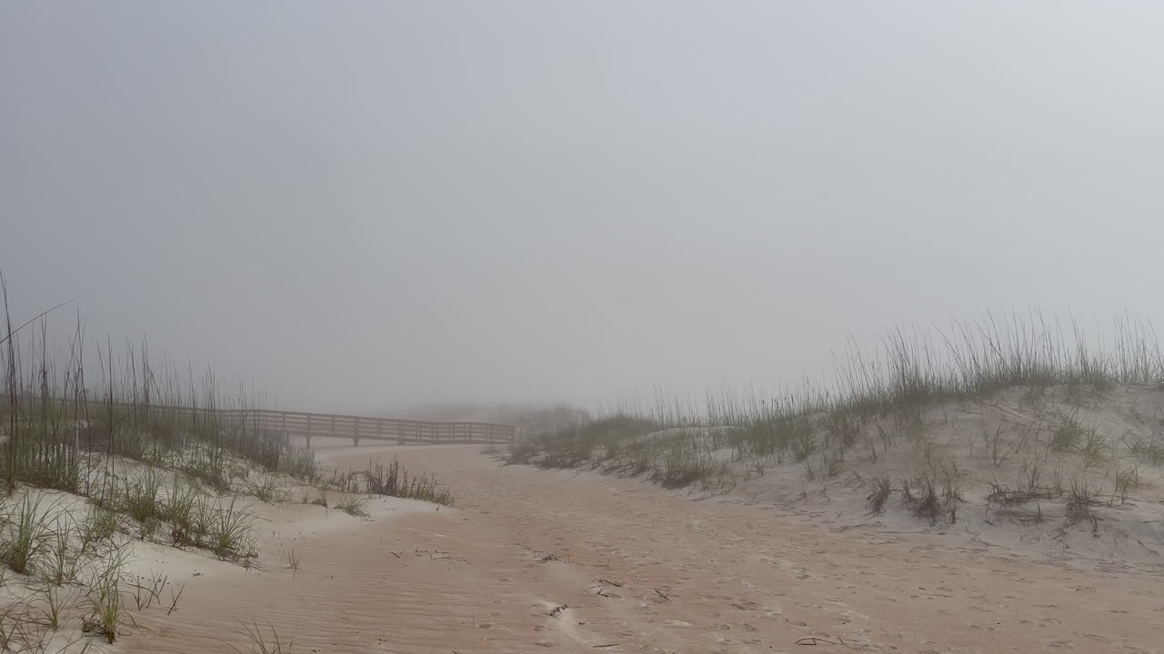 Foggy beach, ocean walkway and sand dunes on misty morning