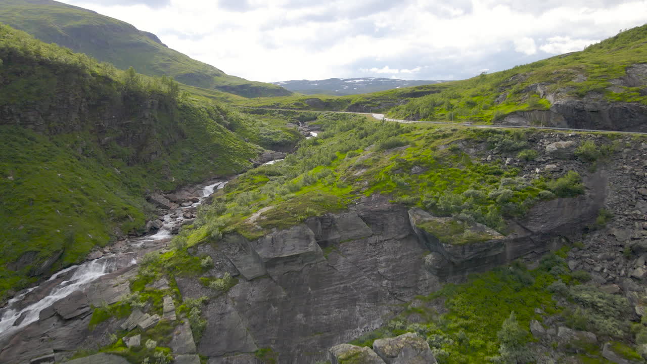 Drone shot rising over a waterfall to reveal a mountain valley landscape, Norway