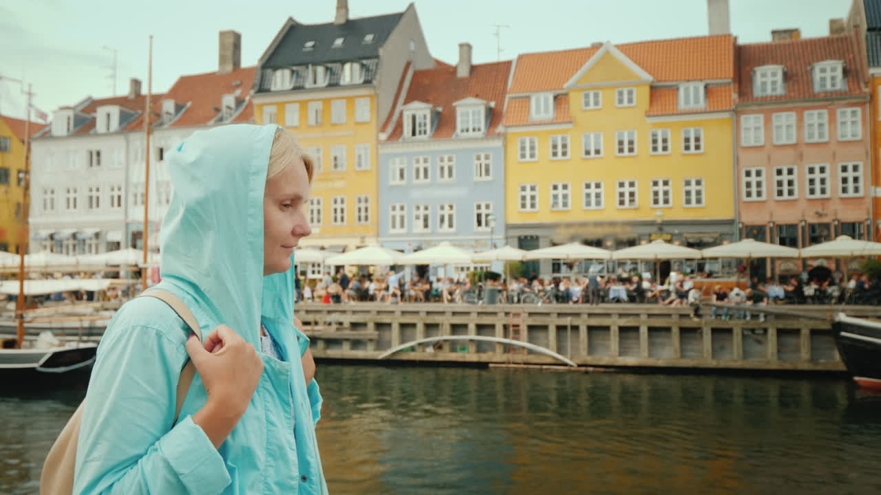 한 여성이 가장 인기 있는 유명한 다채로운 주택을 배경으로 운하를 따라 산책합니다.