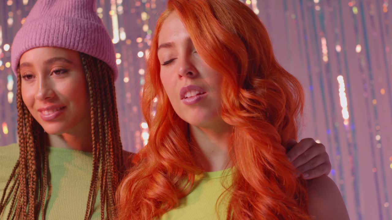 분홍색 배경에 tinsel 커튼 앞에 서있는 두 젊은 gen z 여성의 스튜디오 초상화