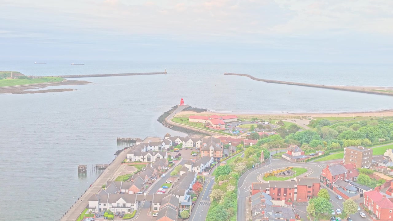 Un drone vola in avanti sopra il Forte Romano di Arbeia, che si affaccia sull'estuario del fiume Tyne a South Shields, Tyne and Wear, Inghilterra, rivelando il Faro di South Pier, l'ingresso del porto, i frangiflutti e il Mare del Nord.
