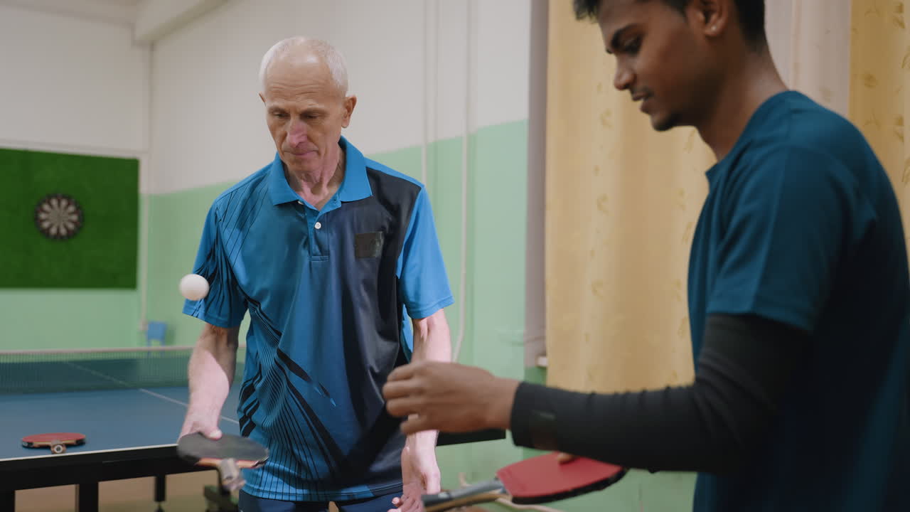 Coach in blue demonstrates technique using racket handle to play tennis while student watches closely, focusing on grip, ball control, teaching moment, and interactive training session
