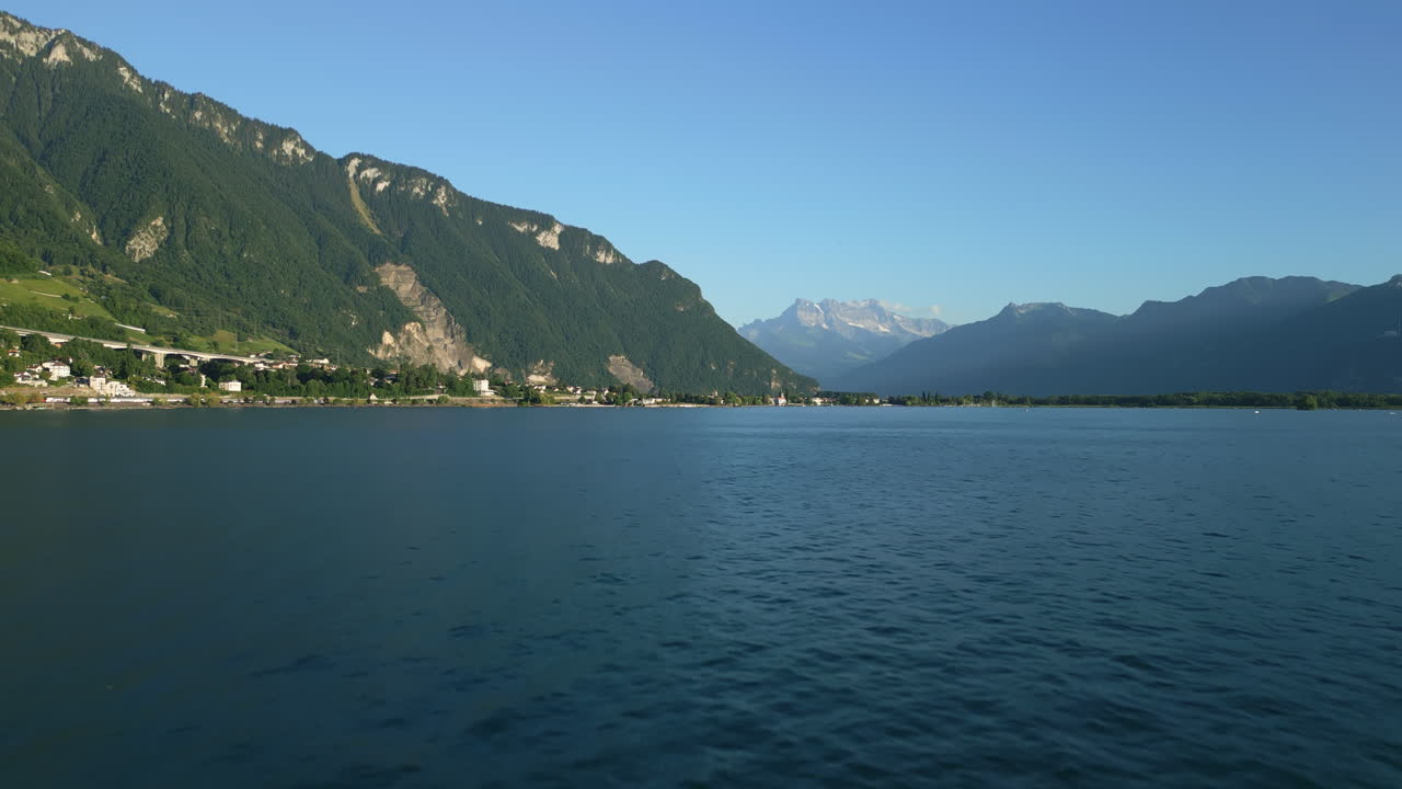 Aerial: Lake Geneva and Dents du Midi at sunset with golden hour colors in canton of Vaud, Switzerland, establishing drone shot