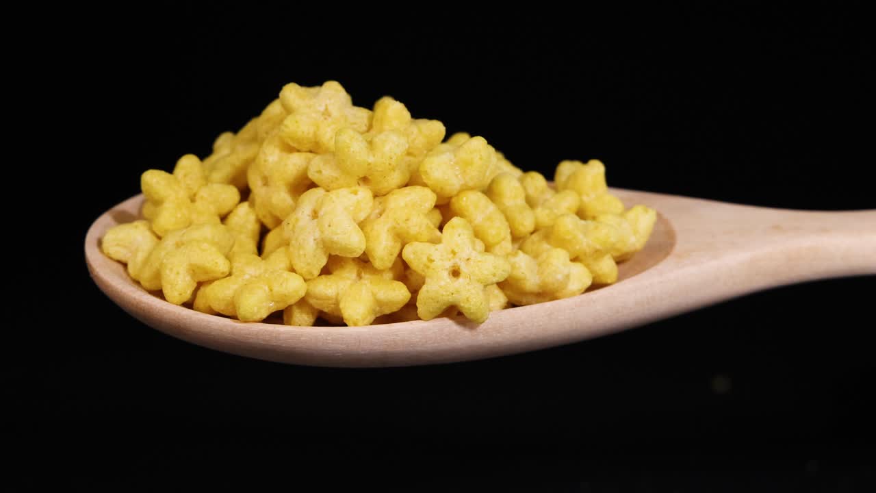 Star-shaped cereal pieces tumble from a wooden spoon against a black background, highlighting texture and motion in a simple setting